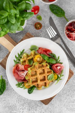 Beyaz tabakta domatesli ıspanaklı waffle, roka ve prosciutto ile bir fincan kahve. Sağlıklı kahvaltı. Üst görünüm.
