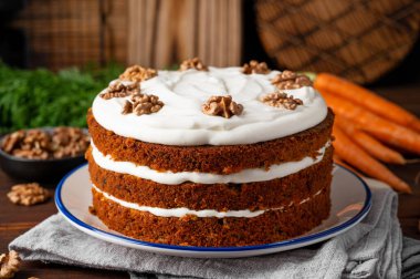 Carrot cake with cinnamon, walnuts and cream cheese frosting on a plate on a dark wooden background. Rustic style. Copy space