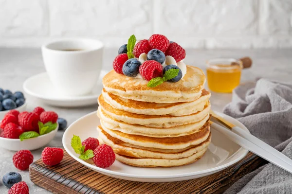 Krem şantili bir yığın krep, taze böğürtlen ve bal gri beton arka planda beyaz bir tabakta.