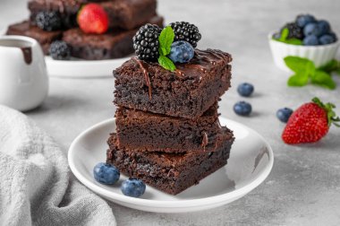 Çikolata kaplı bir yığın browni, gri beton arka planda beyaz bir tabakta taze böğürtlen ve nane yaprakları. Tatlı nefis.