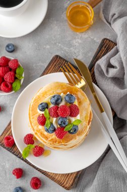 Krem şantili bir yığın krep, taze böğürtlen ve bal gri beton arka planda beyaz bir tabakta.