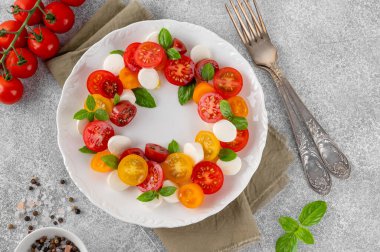 Kiraz domatesli Caprese salatası, mini mozzarella, pesto sosu ve beyaz tabakta taze fesleğen. Sağlıklı vejetaryen yemeği.