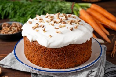 Carrot cake with cinnamon, walnuts and cream cheese frosting on a plate on a dark wooden background. Rustic style. Copy space