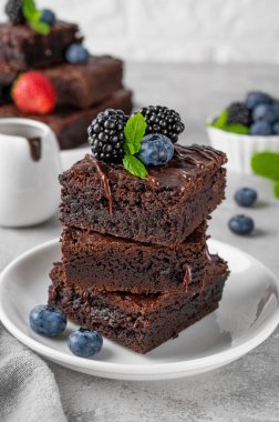 Çikolata kaplı bir yığın browni, gri beton arka planda beyaz bir tabakta taze böğürtlen ve nane yaprakları. Tatlı nefis.