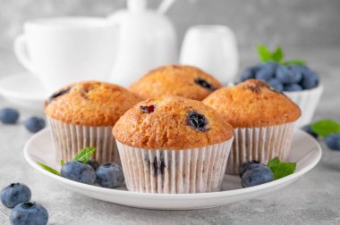 Beyaz tabakta lezzetli yaban mersinli çörekler gri beton arka planda bir fincan çay, taze böğürtlen ve nane yapraklarıyla