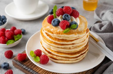 Krem şantili bir yığın krep, taze böğürtlen ve bal gri beton arka planda beyaz bir tabakta.