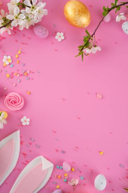 Tavşan Kulaklı Paskalya kompozisyonu, Çikolatalı Yumurtalar, Çiçek açan dallar ve pembe arka planda renkli serpiştirmeler. Üst görünüm, alanı kopyala