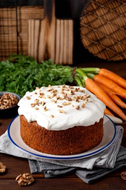 Carrot cake with cinnamon, walnuts and cream cheese frosting on a plate on a dark wooden background. Rustic style. Copy space