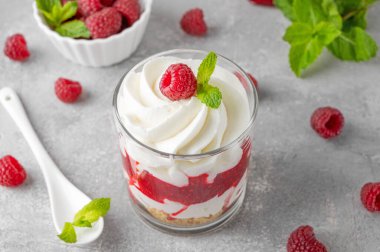 Krem şantili ahududu tatlısı, çilek sosu, kurabiye kırıntıları ve gri beton arka planda bir bardaktaki nane yaprakları. Yaz diyeti tatlısı