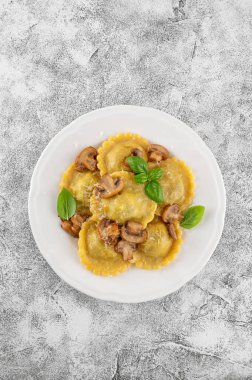 Geleneksel İtalyan İtalyan ravioli makarnası, ricotta, mantar ve parmesan peyniri ile beton arka planda beyaz bir tabakta. Üst görünüm