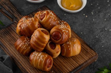 Mini hot dog ısırıkları. Maya hamuru kapağında pişmiş sosisler. Ahşap bir tahtanın üzerinde, koyu beton bir arka planda, battaniyedeki domuzlar. Üst görünüm