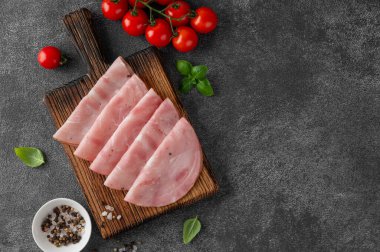 Lezzetli jambon, baharatlar, kiraz domatesleri ve koyu taştan bir arka planda fesleğen yapraklarıyla kesme tahtasının üzerinde yuvarlak dilimler halinde kesilmiş. Üst görünüm