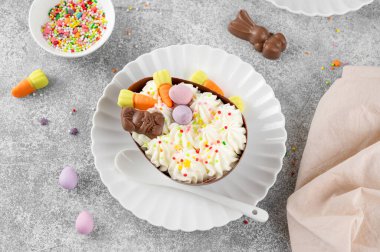 Paskalya tatlısı. Çikolatalı yumurtalar çikolata şekerleri ve şeker parçacıkları ile süslenmiş gri beton arka planda beyaz bir tabakta. Boşluğu kopyala