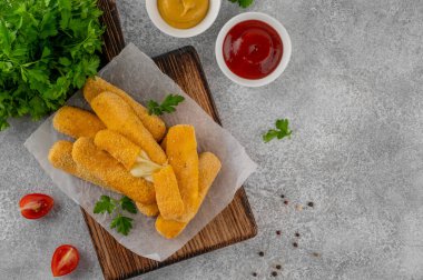Maydanozlu ve ketçap ve hardal soslu gevrek mozzarella çubukları. Altın rengi kızarmış doku, gri arka planda iştah açıcı aperatif. Üst görünüm