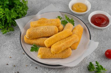 Ketçap ve hardal sosuyla servis edilen maydanozlu bir tabakta kızarmış mozzarella çubukları. Altın rengi kızartılmış doku, gri arka planda iştah açıcı aperatif..