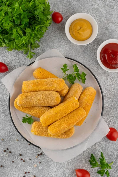Ketçap ve hardal sosuyla servis edilen maydanozlu bir tabakta kızarmış mozzarella çubukları. Altın rengi kızartılmış doku, gri arka planda iştah açıcı aperatif..