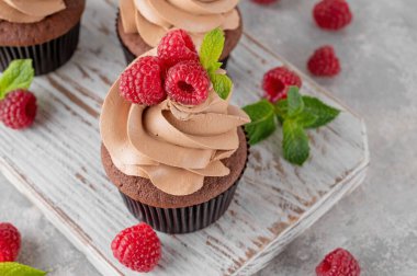 Kremalı çikolatalı kekler taze ahududu ve gri beton arka planda nane yapraklarıyla süslenmiş. Lezzetli bayram tatlısı.