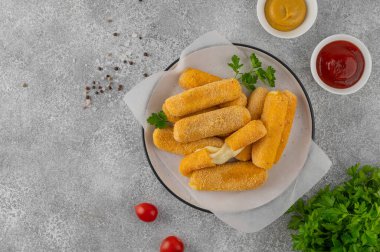 Ketçap ve hardal sosuyla servis edilen maydanozlu bir tabakta kızarmış mozzarella çubukları. Altın rengi kızartılmış doku, gri arka planda iştah açıcı aperatif..