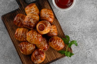 Mini sosisli, hardal ve ketçaplı. Maya hamuru kapağında pişmiş sosisler. Battaniyedeki domuzlar gri arka planda tahta bir tahtanın üzerinde. Üst görünüm, alanı kopyala