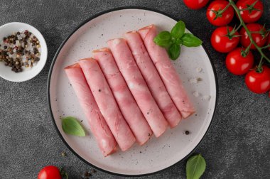 Lezzetli jambon, baharatlar, kiraz domatesleri ve koyu taştan bir arka planda fesleğen yapraklarıyla bir tabakta yuvarlak dilimlenmiş. Üst görünüm