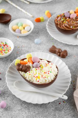 Paskalya tatlısı. Çikolatalı yumurtalar çikolata şekerleri ve şeker parçacıkları ile süslenmiş gri beton arka planda beyaz bir tabakta. Boşluğu kopyala
