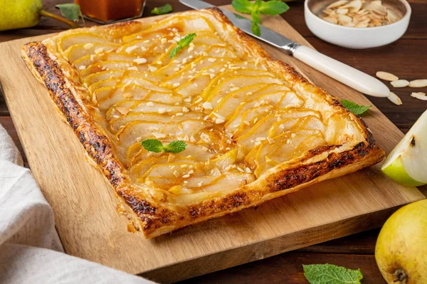 Karamel soslu armut puf böreği ve ahşap zemin üzerinde badem. Lezzetli turta