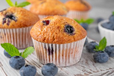 Tahta bir tahta üzerinde lezzetli yaban mersinli çörekler gri bir arka planda bir şişe süt, taze böğürtlen ve nane yapraklarıyla