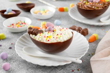 Paskalya tatlısı. Çikolatalı yumurtalar çikolata şekerleri ve şeker parçacıkları ile süslenmiş gri beton arka planda beyaz bir tabakta. Boşluğu kopyala