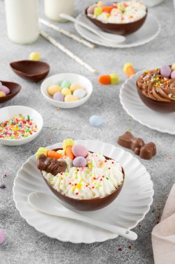 Paskalya tatlısı. Çikolatalı yumurtalar çikolata şekerleri ve şeker parçacıkları ile süslenmiş gri beton arka planda beyaz bir tabakta. Boşluğu kopyala