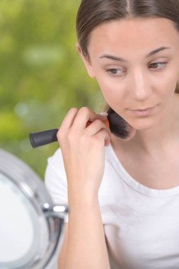 Güzel genç bir kadın yüzüne makyaj yapıyor.