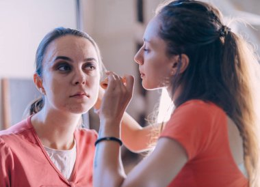 Güzel genç bir kadın aynaya makyaj yapıyor.