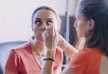 Güzel genç bir kadın aynaya makyaj yapıyor.