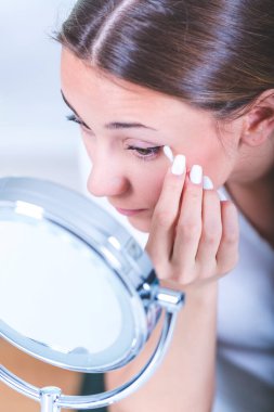 Genç bir kadın banyoda makyaj kremi sürüyor.