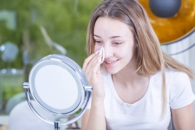 Güzel genç bir kadın yüzüne makyaj yapıyor.