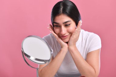 Ayna ve pembe arka planı olan genç bir kadın.