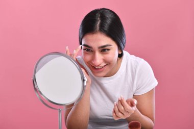 Pembe arka planda makyajı ve aynası olan güzel genç bir kadın.