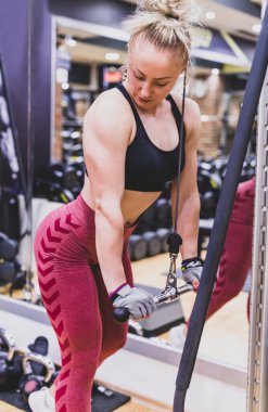 Spor salonunda dambıllarla egzersiz yapan genç bir kadın.