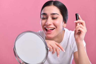 Yüzünde makyaj fırçası olan güzel genç bir kadın ve pembe üzerine izole edilmiş kameraya bakıyor.