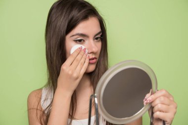 Yüzünde makyaj fırçası olan genç ve güzel bir kadın bej arka planda izole edilmiş.