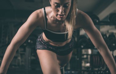 Spor salonunda dambıllarla egzersiz yapan genç bir kadın.