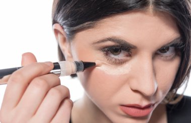 Güzel genç bir kadın yüzüne makyaj yapıyor.