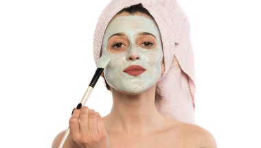 Yüzünde maske olan genç bir kadın yüz kremi sürüyor.