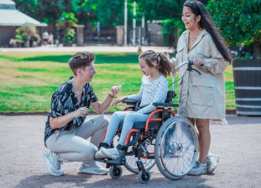 Kızıyla birlikte parkta tekerlekli sandalyede oturan genç bir çift.