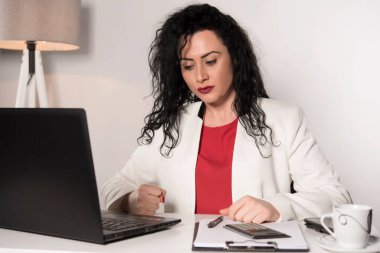 İş yerinde laptopla ve kahveyle çalışan genç bir kadın.