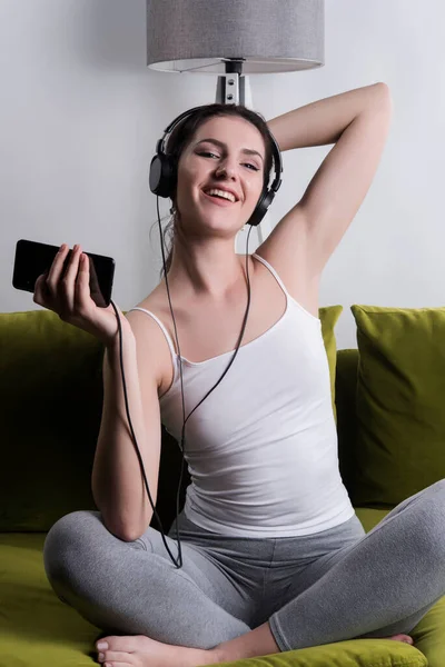 아름다운 여자가 소파에 앉아서 헤드폰을 음악을 미소짓고 — 스톡 사진