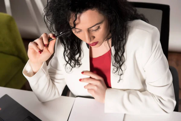 穿着黑色连衣裙 穿着红色夹克 卷曲着头发的年轻貌美的女人正在笔记本电脑上工作 — 图库照片