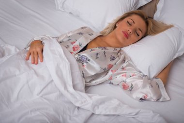 Yatakta uzanmış kameraya bakan güzel bir genç kadın.