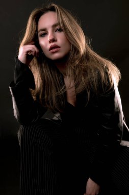 Siyah elbiseli, uzun saçlı, güzel bir kadın. Arka planda poz veriyor.