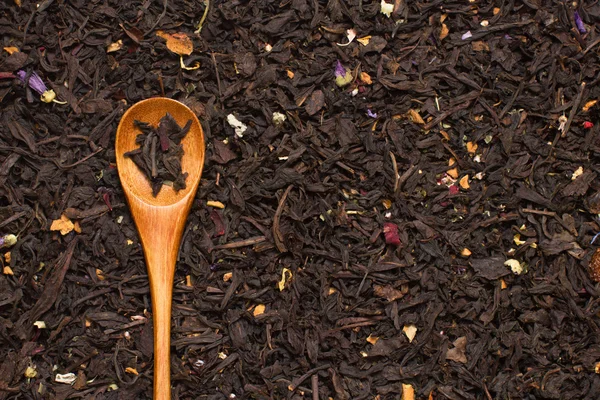 Черный чай листья с цветами и фрукты с деревянной ложкой — стоковое фото