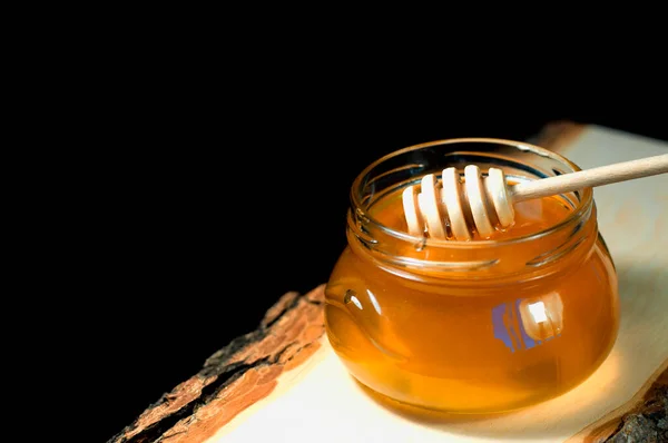 Honey in a jar on a wooden plank on a black background — Stock Photo, Image